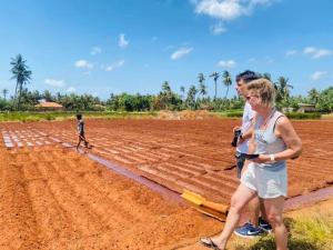 a woman and a man standing on a dirt field with baseball bats at Prasath guest house in Jaffna
