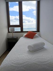 a white bed with a red pillow and a window at Departamentos Terramar in Puerto Montt