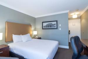 a hotel room with a white bed and a desk at Sandman Hotel Vernon in Vernon