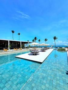 a swimming pool with tables and umbrellas and palm trees at Sofisticação e Luxo à Beira-mar no Cais Eco em Muro Alto by HM in Porto De Galinhas