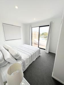 a white bedroom with a bed and a window at Coastal Charm Escape in Karikari Peninsula
