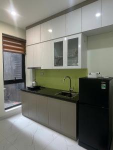 a kitchen with white cabinets and a black refrigerator at Era Apartment Xuân Thuỷ in Hanoi