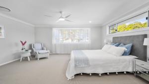 a white bedroom with a bed and a chair at Calypso - Pool, Walk To Beach, Sawtell in Sawtell