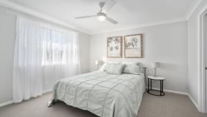 a white bedroom with a bed and a ceiling fan at Calypso - Pool, Walk To Beach, Sawtell in Sawtell