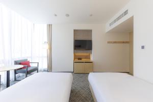 a hotel room with two beds and a table and chair at JR Kyushu Hotel Blossom Shinjuku in Tokyo