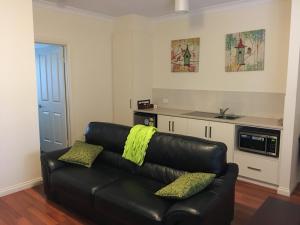 a living room with a black leather couch with yellow pillows at Hahndorf Oak Tree Cottages in Hahndorf