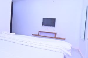 a white room with a bed with a tv on the wall at Shri Ramnarayan Homestay in Prayagraj