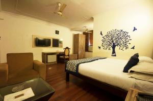 a bedroom with a bed and a chair and a tree on the wall at Golden Leaf Hotel in New Delhi