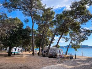 a camper parked next to the water with trees at Camping Park Soline Pitches in Biograd na Moru