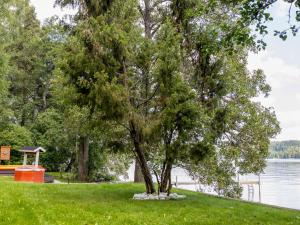 a tree in the grass next to a lake at Holiday Home Lomaranta by Interhome in Paksalo