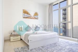 a white bedroom with a bed and a large window at Bloomfields Metropolitan 3br In Bridges in Abu Dhabi