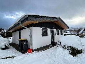 a house covered in snow with a red bucket at Ferienhaus Trüdi 2 - Gemütlicher freistehender Bungalow in Wolfshagen +11 photos