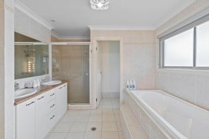 a white bathroom with a tub and a sink at Front Lake View 4Bed Home with Pool and Mins to Mall in Doolandella