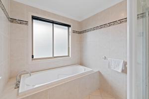 a bathroom with a bath tub and a window at Front Lake View 4Bed Home with Pool and Mins to Mall in Doolandella