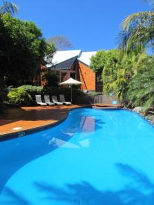 a large blue swimming pool with chairs and a house at Shelly Beach Resort in Port Macquarie