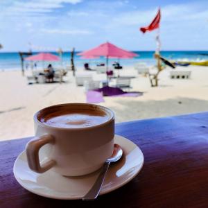 a cup of coffee sitting on a table next to the beach at French garden Pragash Beach Hotel in Trincomalee