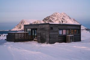 a small house in the snow with a mountain at Designhytte med jacuzzi sentralt i Lofoten in Kleppstad