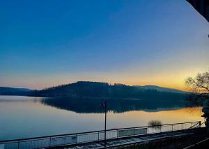 a view of a lake at sunset with a fence at Strandhaus Edersee - Kaminzimmer, Seeblick, Badestrand, Seeterrasse in Waldeck