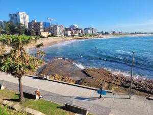 a beach with people walking on a boardwalk next to the ocean at Sunny Apt on The Esplanade - Aircon in Cronulla