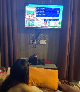 a woman sitting on a bed watching a tv at LJ's escape 2BR COAST Residences in Manila