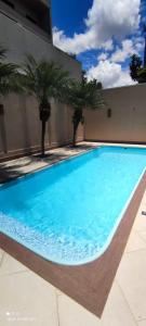 a large blue swimming pool with palm trees in front of a building at A melhor acomodação entre Pinhais e Curitiba - quarto para até O4 pessoas em casa com garagem in Curitiba
