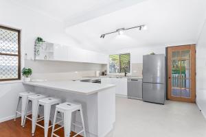 a white kitchen with a large white counter and stools at Perfect Cooee Bay Beach Getaway! in Yeppoon