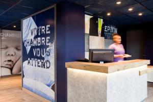 a woman standing behind a counter with a computer at ibis budget Saint-Omer Centre in Saint-Omer