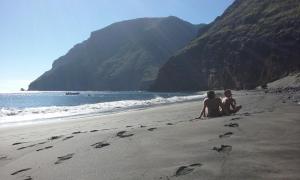 two people sitting on a beach with footprints in the sand at Albergue Montes de Anaga in El Bailadero