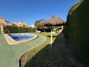 a swimming pool with a straw umbrella next to a yard at Casa Dolce Vita Torrevieja in Torrevieja