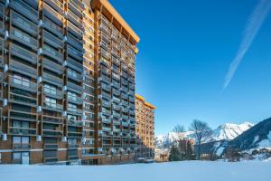 een hoog gebouw in de sneeuw met bergen op de achtergrond bij Le Murmure des Flocons - Vostok Zodiaque in Villarembert
