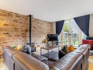 a living room with a leather couch and a brick wall at Beautiful Stone Barn with Hot Tub on a Quiet Farm in Eckington