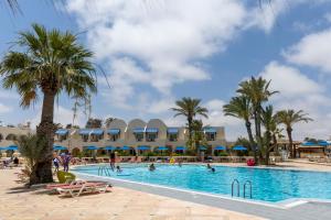 乌姆苏克Le Petit Palais Djerba & Spa的棕榈树的度假泳池和泳池内的人