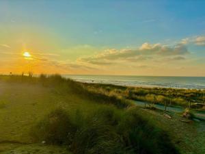 a sunset over a beach with the ocean and grass at Holiday Home Buitenplaats Schouwen nr 86 by Interhome in Burgh Haamstede