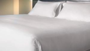 a white bed with white sheets and pillows at NH Córdoba Urbano in Córdoba