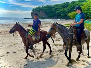a woman and a boy riding horses on the beach at La Veranera, Playa El Coco in San Juan del Sur