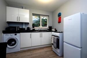 a kitchen with white cabinets and a washer and dryer at Cozy 2-Bed Detached Bungalow with Parking Woking in Horsell