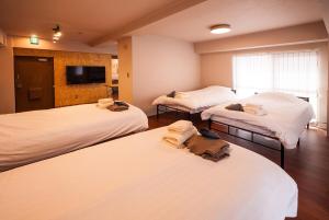 a hotel room with three beds and a flat screen tv at TABiTO Stay Inarimachi in Toyama