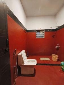 a bathroom with a toilet and a red wall at Amberleaf Estate 4BHK Homestay Coorg by Homeyhuts in Virajpet +39 photos