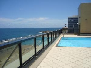 a swimming pool on top of a building next to the ocean at Farol Barra Flat 202 in Salvador