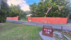 a sign in a yard next to a brick wall at 古民家コテージ やんばるの家 Yanbaru no ie "美ら海水族館まで徒歩14分 "雨天でもテラスでBBQが楽しめます "詳しくはホスト情報より" in Motobu