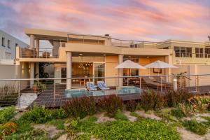 una casa en la playa con sillas y sombrillas en "Villa Montemar' Luxury Villa for 6 on the Beach with Pool, en Gordonʼs Bay
