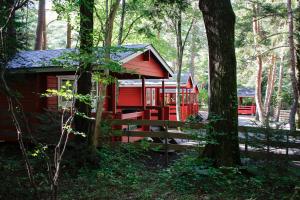 a red cabin in the woods with a fence at PICA Fujiyoshida in Fujiyoshida