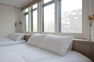 a bed with white pillows in a room with windows at Manso Hostel in DDP in Seoul