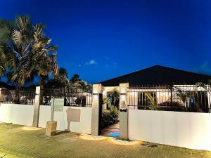 a white fence with a gate and a palm tree at Eagle Stays Aruba-NEW Luxurious One Bedroom Apartment Near Eagle Beach! in Oranjestad