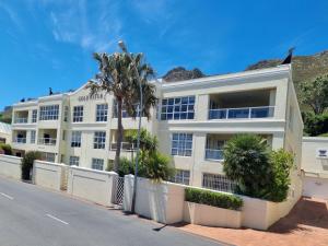 un edificio blanco con una palmera frente a una calle en 'Goldwater on Beach' - 3 Bedroom Beachfront with Balcony & BBQ - Sleeps 6, en Gordonʼs Bay