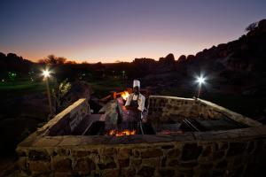 Ein Mann steht nachts neben einer Feuerstelle in der Unterkunft Gondwana Canyon Lodge in Kanebis