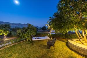 DebāriELIVAAS Cows & Cuddles 4 BHK with Pvt Pool and Garden的坐在树旁的草上长凳