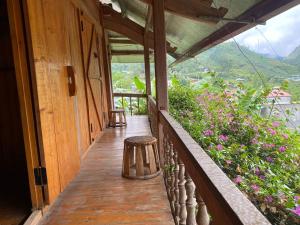 un porche de madera con un taburete y algunas flores en Homestay Loan Ươi, en Bắc Hà