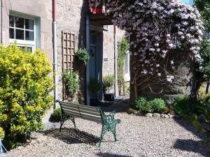 a bench sitting in front of a building with flowers at Wee Ness Cottage in Inverness