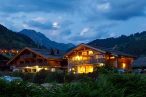 uma casa de madeira à noite com montanhas ao fundo em Chalet-Hotel et Spa Le Delta em Le Grand-Bornand